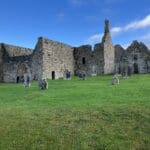 Here's an alt tag for the image: Ruined monastery with Celtic cross and graves.